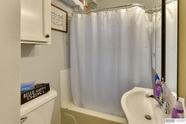 bathroom featuring a sink, toilet, and shower / tub combo with curtain