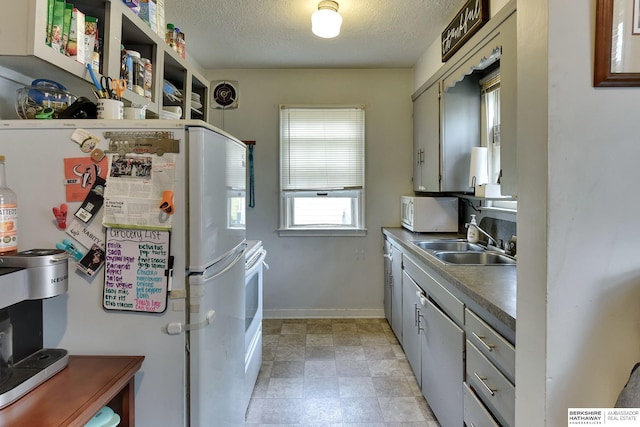 kitchen with visible vents, white appliances, baseboards, a textured ceiling, and a sink