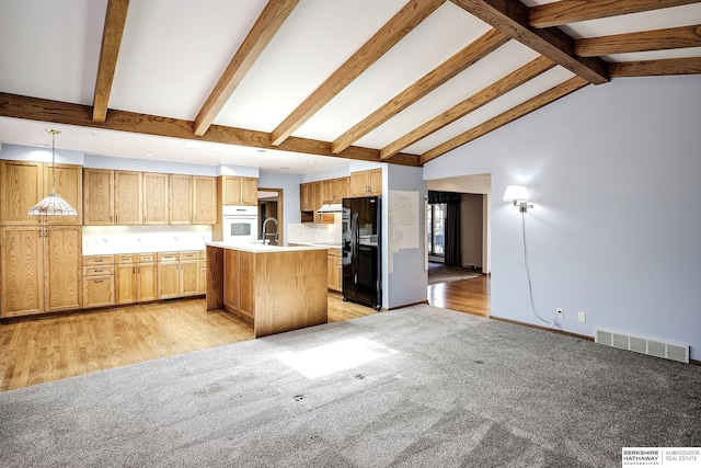 kitchen featuring black fridge with ice dispenser, visible vents, beam ceiling, an island with sink, and light countertops