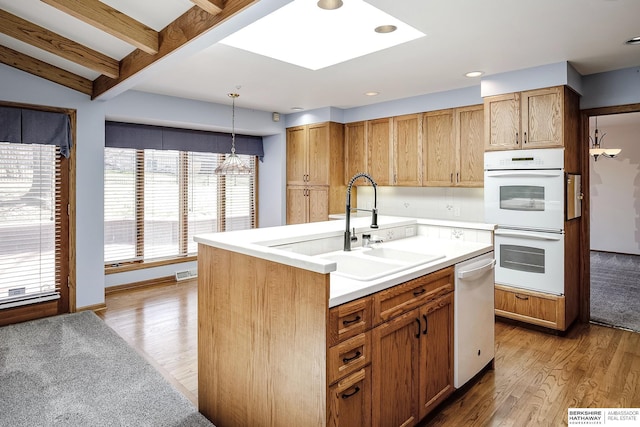 kitchen featuring decorative light fixtures, a sink, light countertops, light wood-style floors, and white appliances