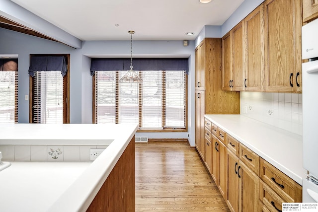 kitchen featuring brown cabinetry, backsplash, hanging light fixtures, light countertops, and light wood finished floors