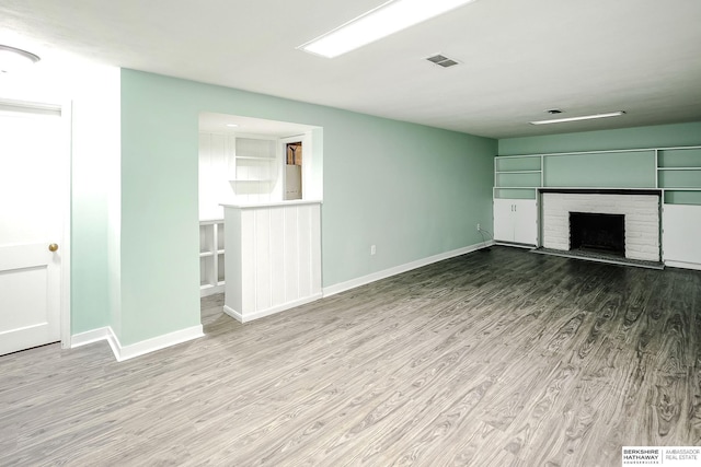 unfurnished living room with baseboards, a fireplace with raised hearth, wood finished floors, and visible vents