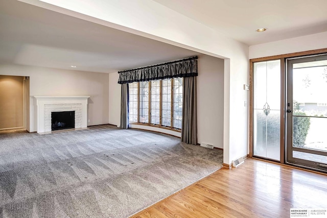 unfurnished living room featuring baseboards, a fireplace with flush hearth, wood finished floors, and visible vents