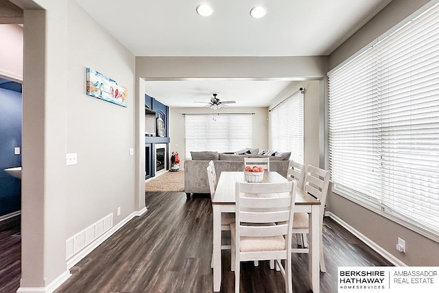 dining room featuring a glass covered fireplace, a ceiling fan, dark wood finished floors, and visible vents