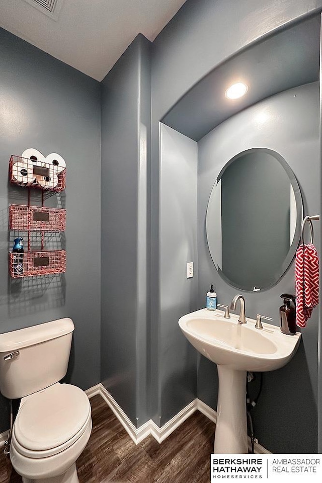 half bathroom with baseboards, wood finished floors, and toilet