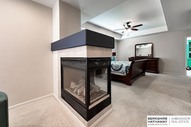 carpeted bedroom with baseboards, ceiling fan, a tray ceiling, and a fireplace