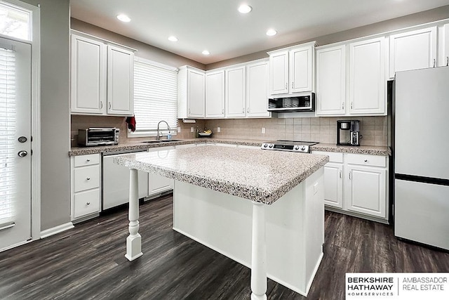 kitchen with a kitchen island, appliances with stainless steel finishes, a sink, white cabinets, and dark wood-style floors