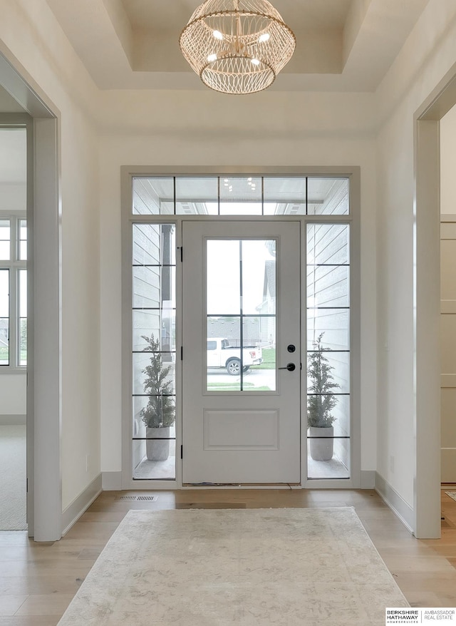 entryway featuring baseboards, a chandelier, light wood-style flooring, and visible vents