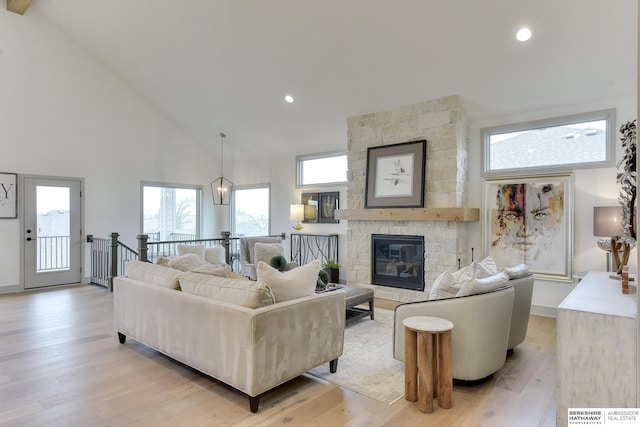 living area with light wood-type flooring, recessed lighting, high vaulted ceiling, and a stone fireplace