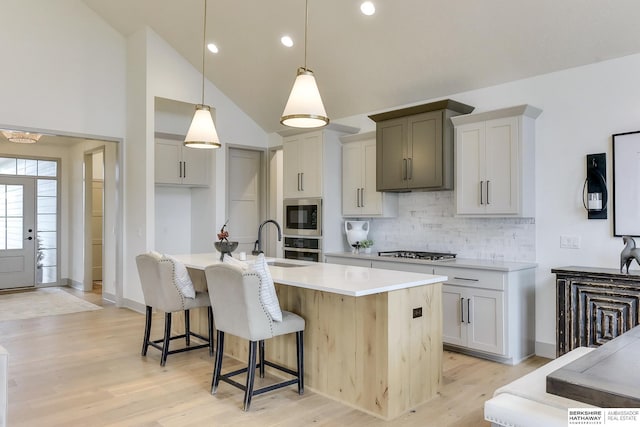 kitchen with appliances with stainless steel finishes, light wood finished floors, light countertops, tasteful backsplash, and a center island with sink