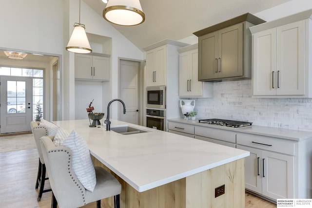 kitchen featuring decorative backsplash, a kitchen island with sink, a sink, light countertops, and stainless steel appliances