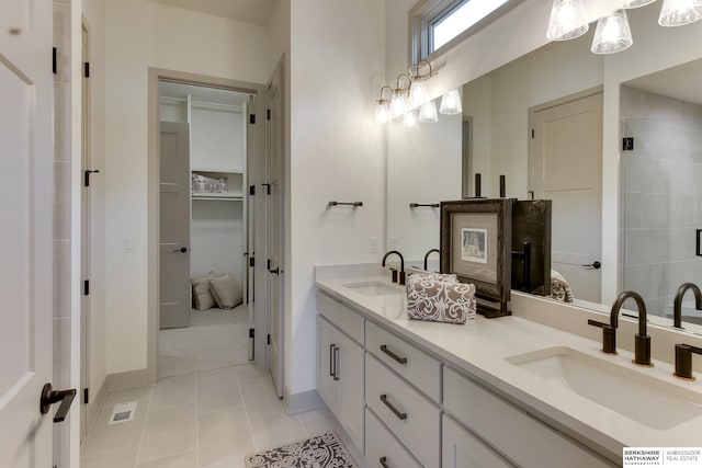 bathroom with double vanity, a sink, tile patterned flooring, and tiled shower