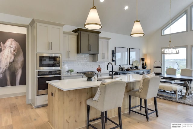 kitchen featuring light countertops, a sink, a kitchen island with sink, and oven