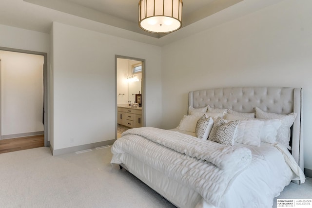 bedroom featuring a sink, baseboards, ensuite bathroom, and light colored carpet