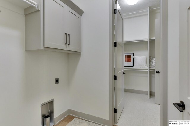 laundry room featuring cabinet space, hookup for an electric dryer, baseboards, and light wood finished floors