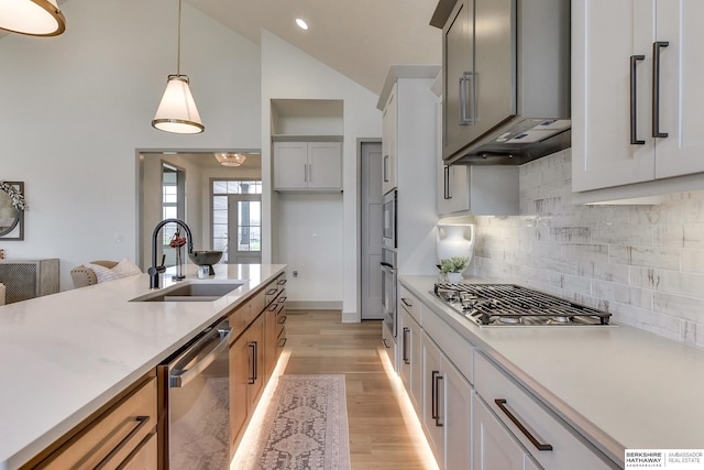 kitchen with appliances with stainless steel finishes, a sink, light countertops, decorative light fixtures, and light wood-type flooring