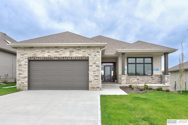 prairie-style home with a front lawn, concrete driveway, an attached garage, a shingled roof, and stone siding