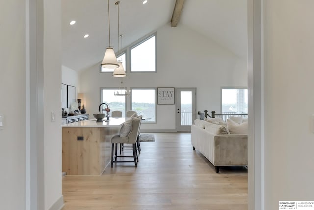 kitchen with a breakfast bar, beam ceiling, light wood finished floors, light countertops, and high vaulted ceiling