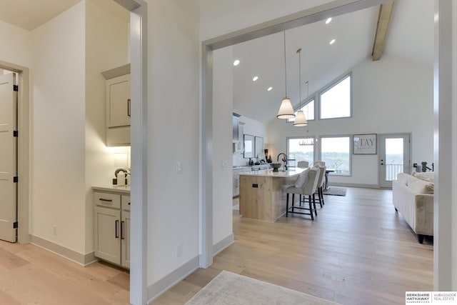 interior space featuring beamed ceiling, open floor plan, a kitchen breakfast bar, high vaulted ceiling, and light wood-type flooring