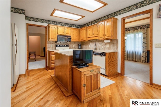 kitchen with light wood finished floors, white appliances, light countertops, a center island, and tasteful backsplash