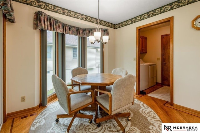 dining area featuring separate washer and dryer, baseboards, a notable chandelier, and light wood-type flooring