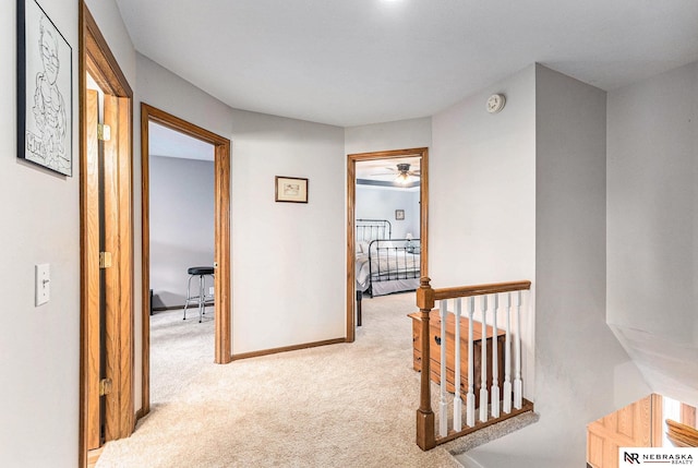 hall featuring baseboards, light carpet, and an upstairs landing