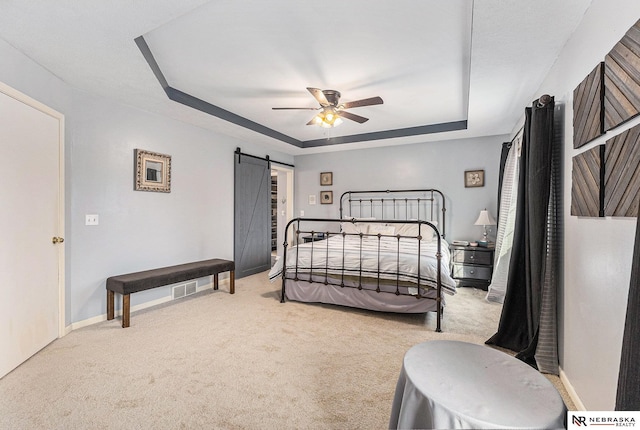 carpeted bedroom with a ceiling fan, a tray ceiling, a barn door, and baseboards