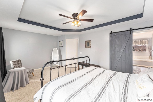 carpeted bedroom featuring baseboards, a barn door, a ceiling fan, and a tray ceiling