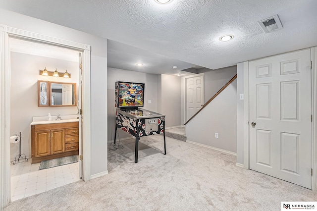 interior space featuring a textured ceiling, light colored carpet, visible vents, a sink, and baseboards
