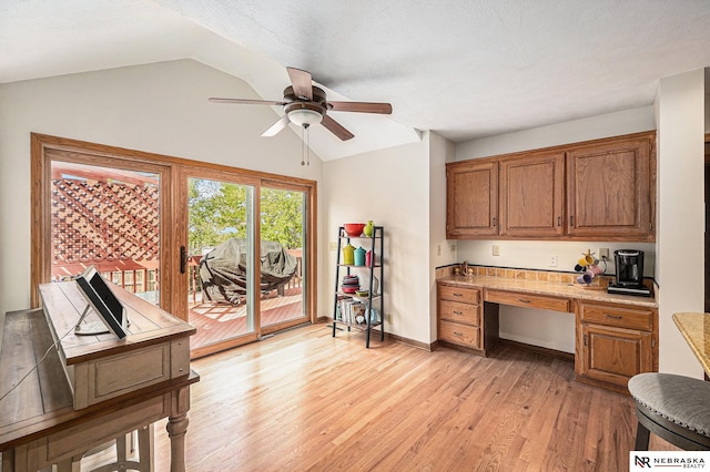 office featuring ceiling fan, built in desk, baseboards, light wood-type flooring, and vaulted ceiling
