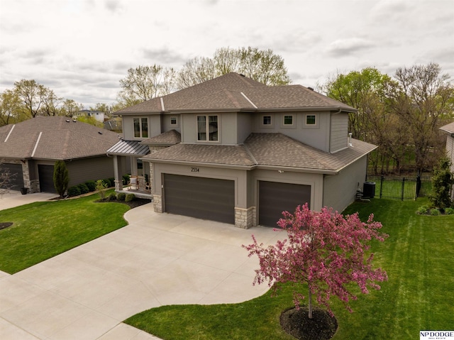 prairie-style home with driveway, fence, a front lawn, an attached garage, and stucco siding