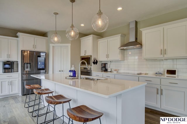 kitchen with a kitchen breakfast bar, wall chimney range hood, recessed lighting, tasteful backsplash, and appliances with stainless steel finishes