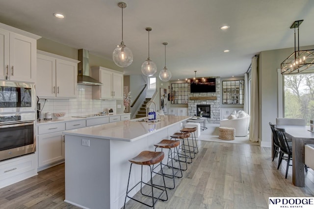 kitchen with a sink, light wood finished floors, a fireplace, wall chimney exhaust hood, and open floor plan