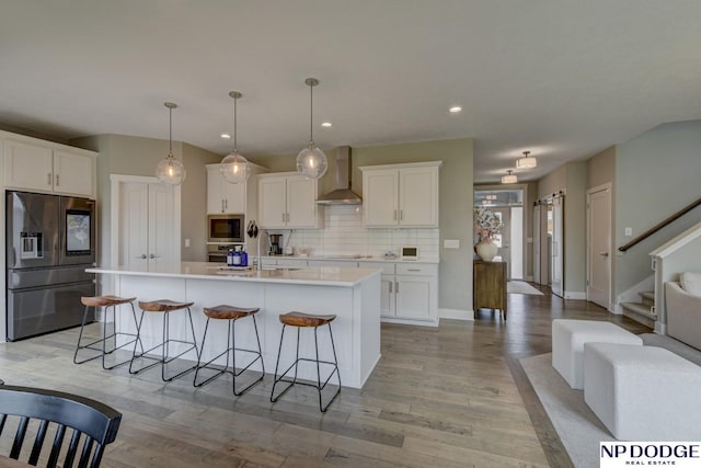 kitchen featuring decorative backsplash, a kitchen island with sink, wall chimney range hood, white cabinets, and stainless steel appliances