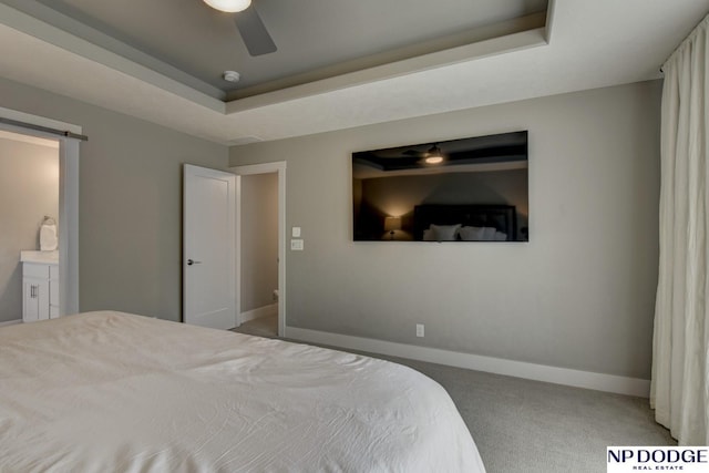 carpeted bedroom with connected bathroom, a barn door, a raised ceiling, a ceiling fan, and baseboards