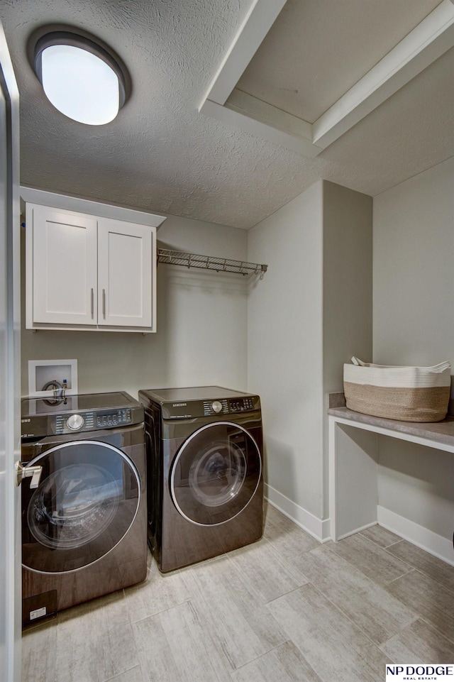 clothes washing area with cabinet space, a textured ceiling, light wood-style flooring, baseboards, and washing machine and dryer