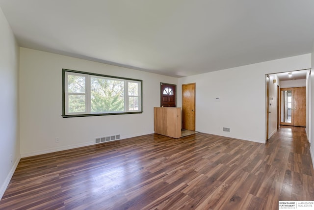 unfurnished living room featuring baseboards, dark wood-style floors, plenty of natural light, and visible vents