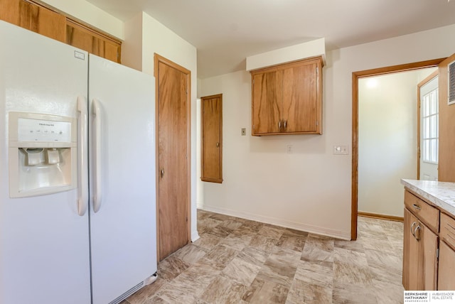 kitchen with light countertops, brown cabinetry, and white fridge with ice dispenser