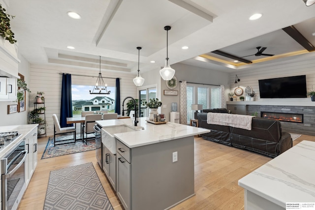 17026 Emma St, Bennington, NE 68007 - kitchen featuring a glass covered fireplace, a raised ceiling, a sink, ceiling fan with notable chandelier, and gray cabinetry