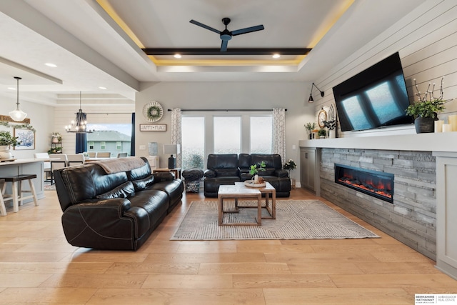 17026 Emma St, Bennington, NE 68007 - living area with a stone fireplace, a raised ceiling, ceiling fan with notable chandelier, light wood-style floors, and recessed lighting
