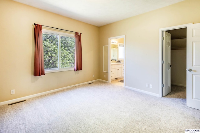 unfurnished bedroom featuring a walk in closet, baseboards, light colored carpet, and visible vents
