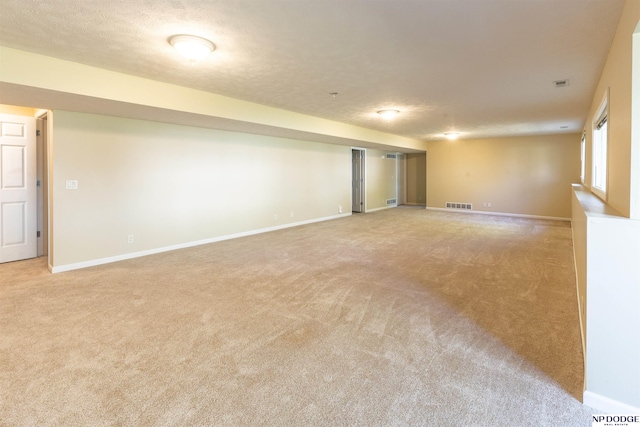 basement featuring light colored carpet, baseboards, visible vents, and a textured ceiling