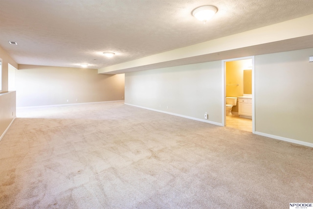 finished below grade area featuring light colored carpet, a textured ceiling, and baseboards