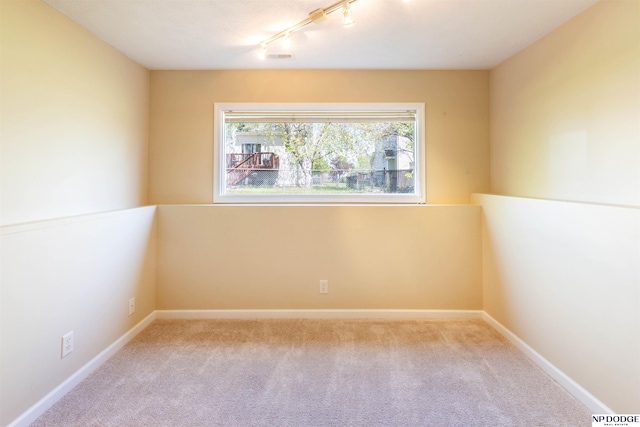 spare room featuring carpet flooring, baseboards, and track lighting