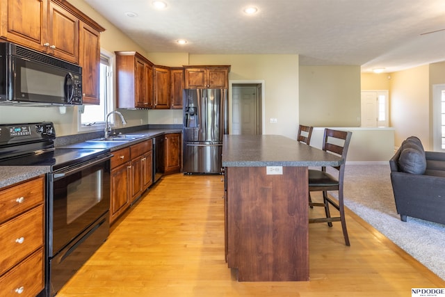 kitchen with a breakfast bar area, a kitchen island, dark countertops, black appliances, and open floor plan