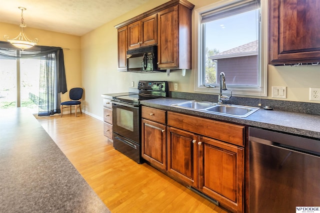 kitchen featuring dark countertops, a sink, black appliances, and light wood-style floors
