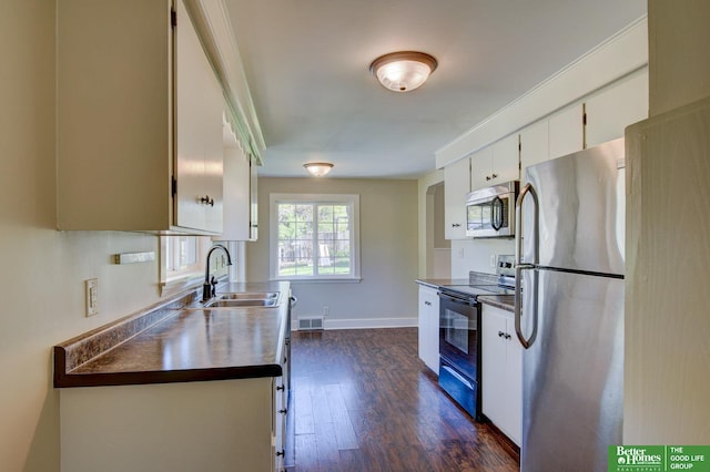 kitchen with a sink, dark countertops, stainless steel appliances, dark wood finished floors, and white cabinetry