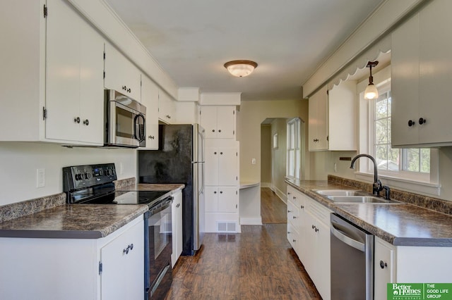 kitchen with dark wood-style flooring, a sink, white cabinetry, dark countertops, and appliances with stainless steel finishes