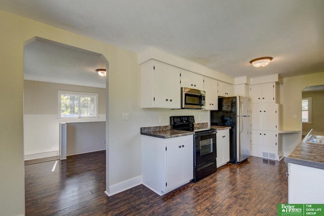 kitchen with arched walkways, dark countertops, stainless steel appliances, and dark wood-type flooring