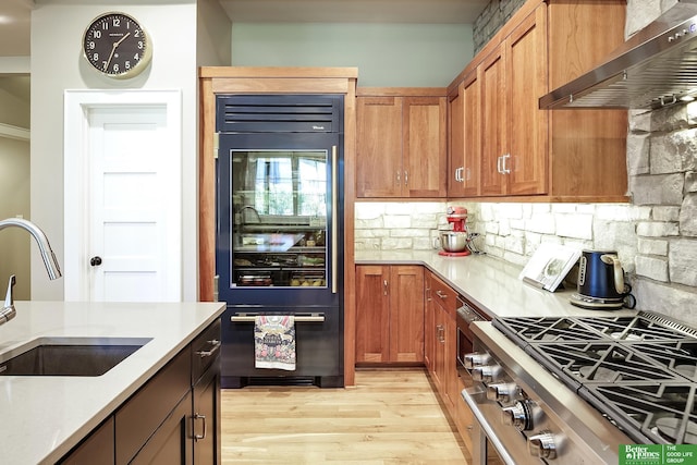 kitchen featuring a sink, stainless steel gas stove, light wood-style flooring, wall chimney exhaust hood, and refrigerator